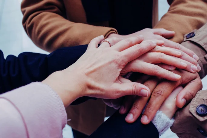 Eine Nahaufnahme von mehreren übereinander gestapelten Händen, die Teamwork, Einheit und Zusammenarbeit innerhalb einer heterogenen Gruppe symbolisieren.