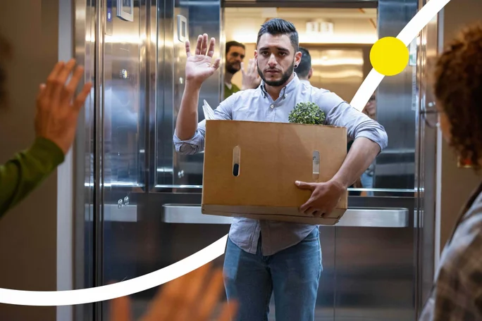 Ein Mann verlässt das Büro mit einem Umzugskarton und verabschiedet sich von Kollegen
