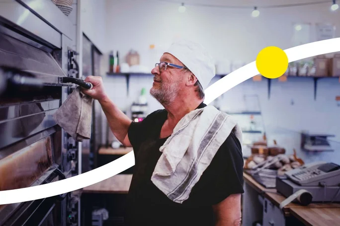 Ein Mann mit einem weißen Hut legt Brot in einen Ofen. Auri - Der Stromanbieter für dein Unternehmen.