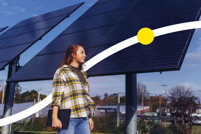 Junge Frau mit kariertem Hemd und Tablet steht vor Solarpanels bei sonnigem Himmel